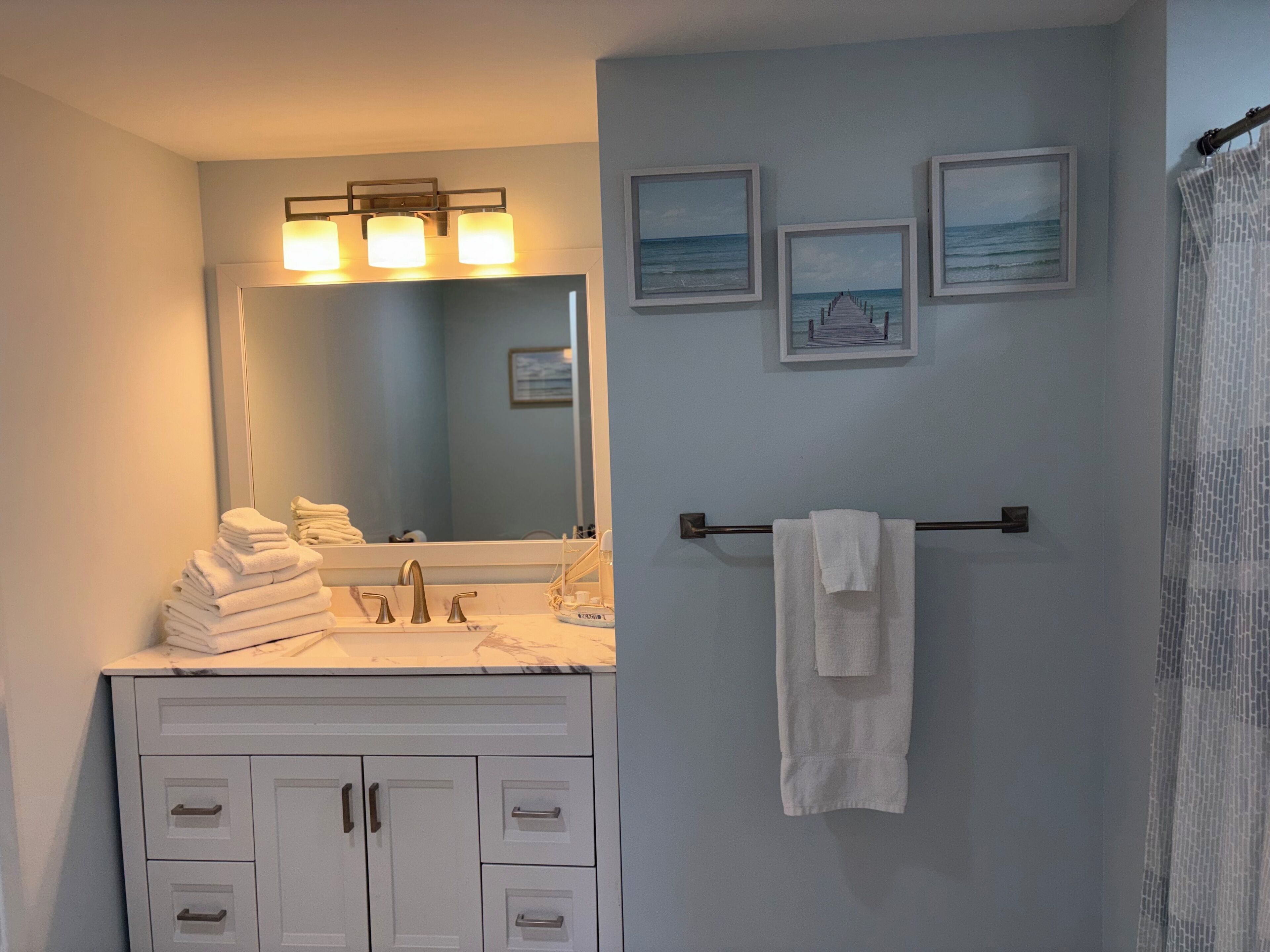 Une salle de bain avec un lavabo, un miroir, un porte-serviettes et trois tableaux encadrés accrochés au mur.