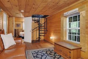 Interior de una cabaña de madera con una escalera, un sofá, un armario y una ventana con vistas.
