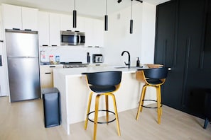 A modern kitchen with white cabinets, stainless steel appliances, black bar stools, and pendant lighting.