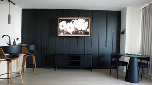 Ein modernes Wohnzimmer mit einer schwarzen Unterhaltungseinheit, einem gerahmten Blumenbild und einem Essbereich mit einem runden Tisch und Stühlen.