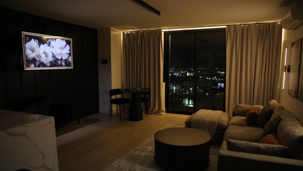 Ein Wohnzimmer mit großem Fernseher, einer Couch, einem Couchtisch und Blick auf die Stadt durch eine Schiebetür.