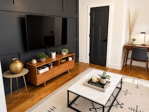 A modern living room with a flat-screen TV, wooden entertainment unit, and a coffee table with a tray. -     Stylish Retreat Near Downtown (Atlanta)