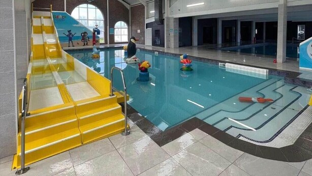 Una piscina interior amb una plataforma de llançament groga, aigua cristal·lina i un sostre alt amb conductes a la vista.