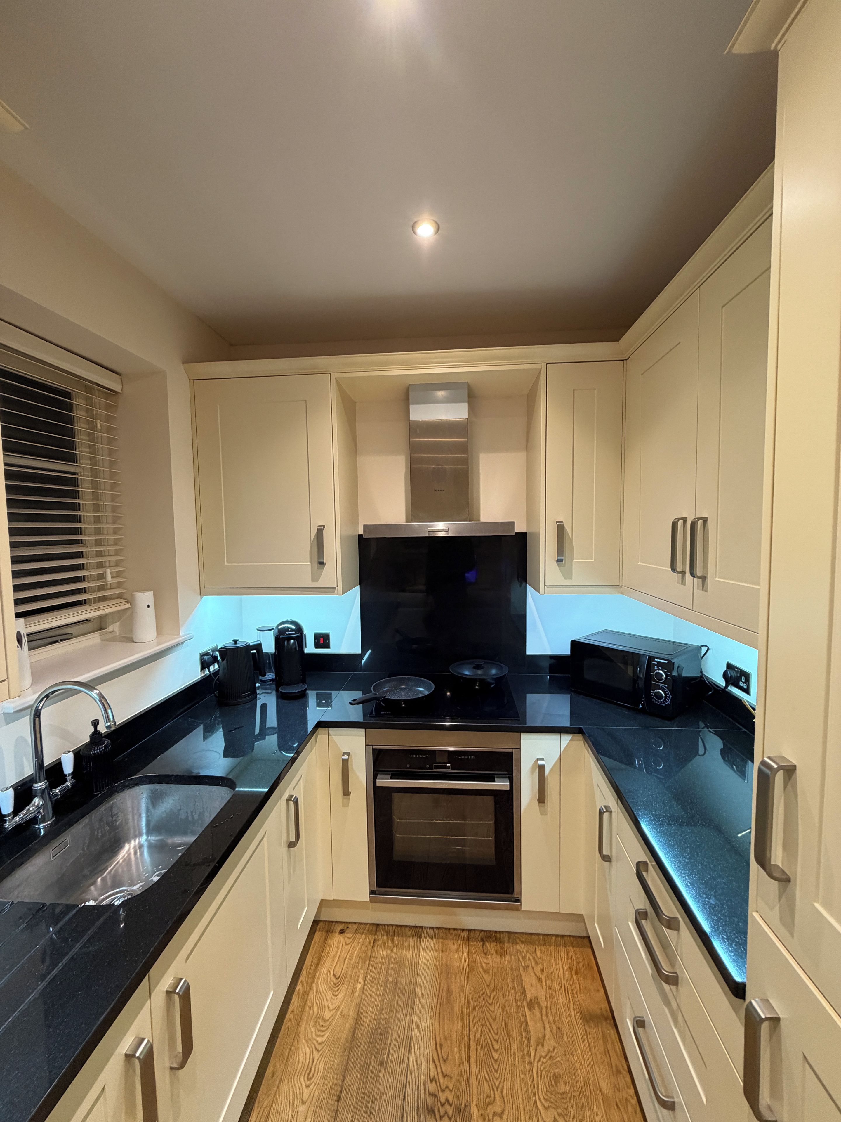 A modern kitchen with white cabinets, a black countertop, a built-in oven, and a microwave.