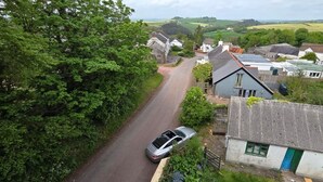 Eine ländliche Straße mit Häusern, einem Auto und viel Grün.