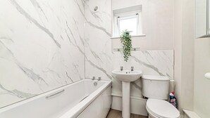 Ett badrum med badkar, handfat, toalett och ett fönster med en växt i.