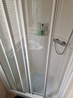 A shower with a glass door, a white sink, and toiletries on the wall. - Caravan Sleeps 8 Pets Welcome wifi (Skegness)