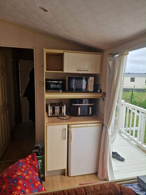 A compact kitchenette with a microwave, toaster, and bread container, a small refrigerator, and a view of a fenced outdoor area. - Caravan Sleeps 8 Pets Welcome wifi (Skegness)