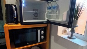 Una cocina compacta equipada con microondas, cafetera y un pequeño estante con tazas y una planta.