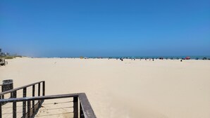 Ein Strand mit blauem Himmel, sandigem Ufer und einigen Sonnenschirmen.