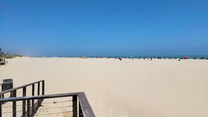 Ein Strand mit blauem Himmel, sandigem Ufer und einigen Sonnenschirmen.