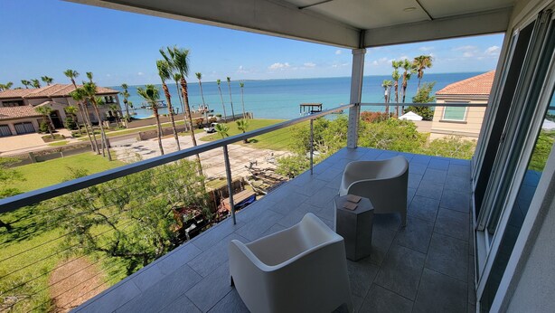 Ein Balkon mit zwei Stühlen, einem Tisch und Blick auf das Meer und Palmen.