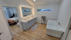 Ein modernes Badezimmer mit einer großen Badewanne, einem Waschtisch mit Spiegel und einem kleinen Fenster.