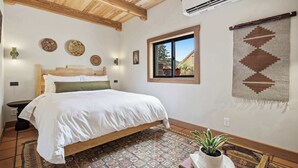 Een slaapkamer met een houten bed, een raam met uitzicht, een kamerbreed tapijt met dessin en een wandairconditioner.