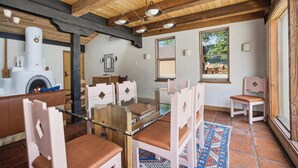 Een rustiek interieur met een open haard, houten balken in het plafond en een eethoek met witte stoelen en een glazen tafel.