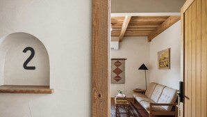 Een kamer met een houten deur, een bord met het nummer 2, een bank, een kamerkleed met een patroon en een wandlamp.