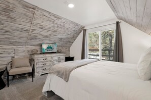 Ein Schlafzimmer mit Bett, Schminktisch, Sessel, Fernseher und Fenster mit Blick auf Bäume.