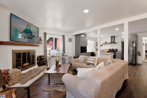 Ein Wohnzimmer mit Kamin, einer Couch und Blick in die Küche.