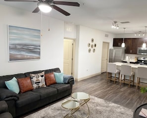 A modern living room with a black sofa, a glass coffee table, and a ceiling fan. - 2 BR Suite in the Heart of Southside • Pool • Gym (Jacksonville)