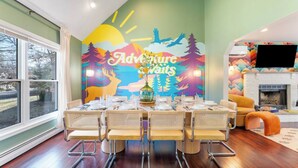 A dining area with a table set for four, a mural with 'Adventure Awaits' text, and a fireplace in the background. - Heated Pool, Mini Golf, Bowling, Hot Tub, GameRoom (East Stroudsburg)