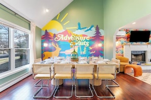 A dining area with a table set for four, a mural with 'Adventure Awaits' text, and a fireplace in the background. - Heated Pool, Mini Golf, Bowling, Hot Tub, GameRoom (East Stroudsburg)