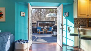 A room with teal walls, a wooden floor, a sofa, a chair, a basket, and a view of an outdoor deck with a table and chairs. - Heated Pool, Mini Golf, Bowling, Hot Tub, GameRoom (East Stroudsburg)