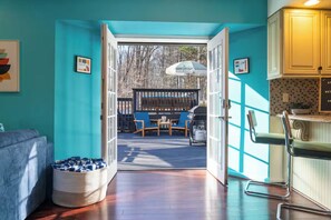 A room with teal walls, a wooden floor, a sofa, a chair, a basket, and a view of an outdoor deck with a table and chairs. - Heated Pool, Mini Golf, Bowling, Hot Tub, GameRoom (East Stroudsburg)