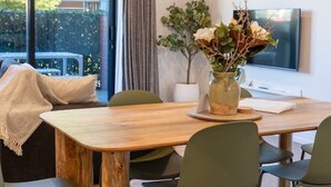 En spiseplads med et træbord, fire stole, en vase med blomster og et fjernsyn på væggen.