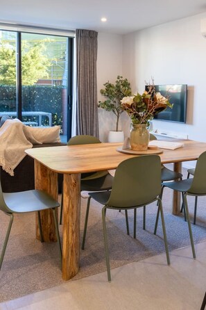 A dining area with a wooden table, four chairs, a vase with flowers, and a television on the wall. - Spacious CBD Townhouse | Stadium + Parking (Christchurch)