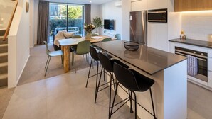 Et moderne køkken med en central ø, spiseområde med stole, og en trappe.