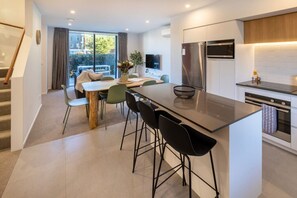 A modern kitchen with a central island, dining area with chairs, and a staircase. - Spacious CBD Townhouse | Stadium + Parking (Christchurch)