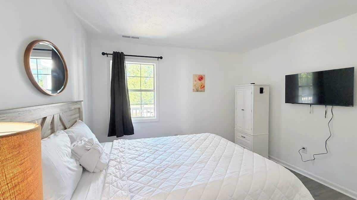 A bedroom with a bed, a television, a wardrobe, and a window with curtains.