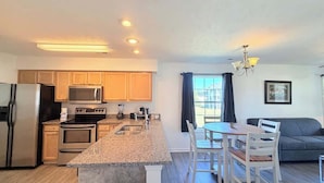 A modern kitchen with granite countertops, stainless steel appliances, and a dining area with a table and chairs. - Spacious 2BR Getaway in Myrtle Beach, Tennis, Pool (Myrtle Beach)