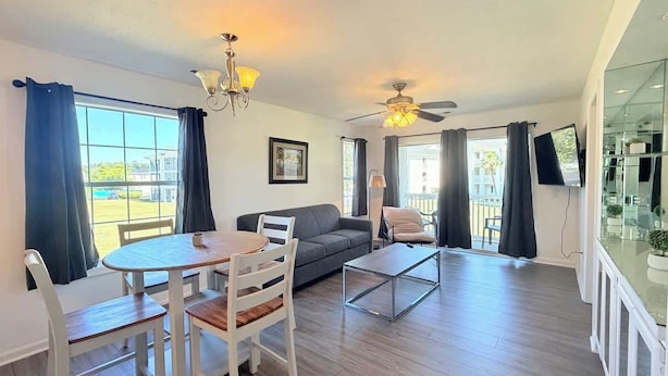 A modern living room with a sofa, a dining table with chairs, a coffee table, a ceiling fan, and a TV mounted on the wall. - Spacious 2BR Getaway in Myrtle Beach, Tennis, Pool (Myrtle Beach)