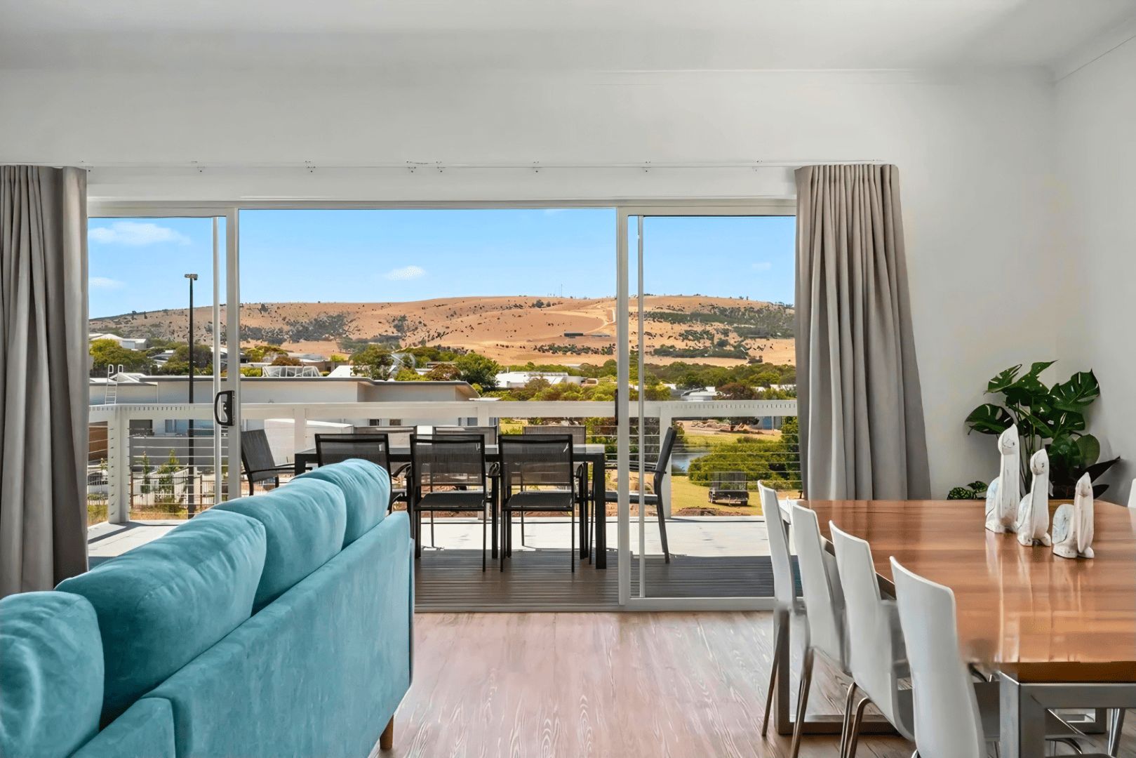 Un salon moderne comprenant un canapé, une table à manger, des chaises et offrant une vue sur un paysage vallonné grâce à de grandes portes-fenêtres coulissantes.