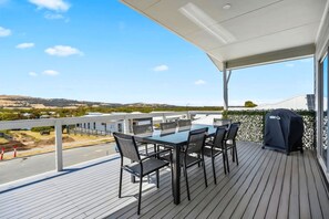 A covered outdoor patio with a table and chairs, a barbecue grill, and a view of a road and distant landscape.