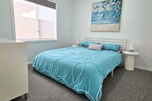 A bedroom with a bed, a nightstand, a bedside lamp, a window, and a painting on the wall.
