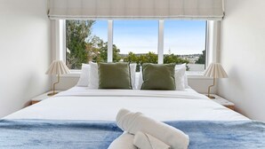 A bedroom with a large bed, two pillows, a view of the outdoors, and two bedside lamps. - Forrest Hill Oasis with Pool, Spa and BBQ (Auckland North Shore)