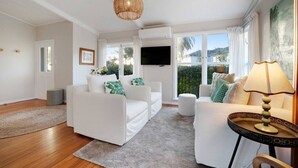 A modern living room with white furniture, a large window, and a flat-screen TV. - Forrest Hill Oasis with Pool, Spa and BBQ (Auckland North Shore)