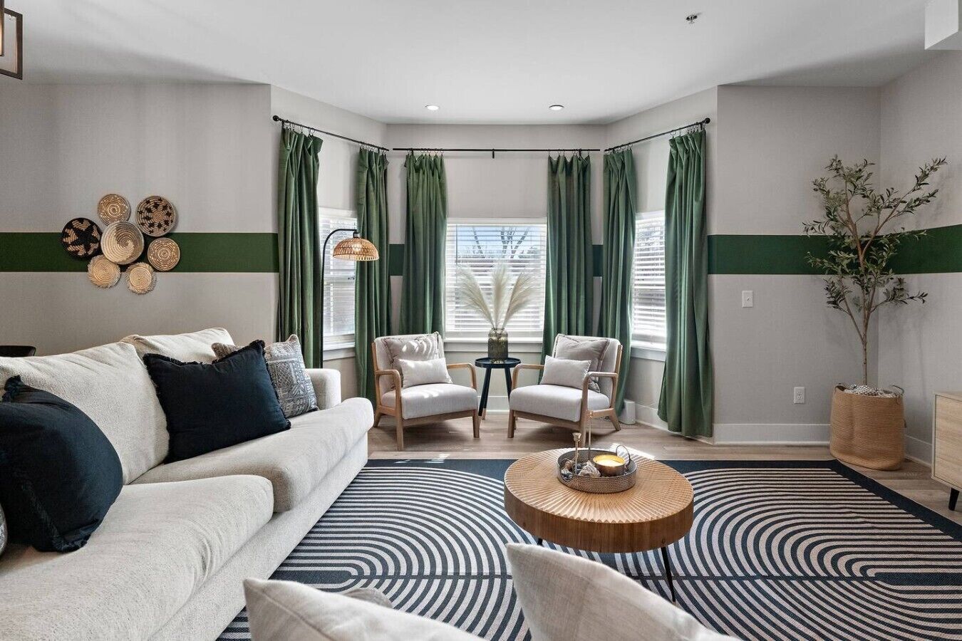 A modern living room with a sofa, two armchairs, a coffee table, and a large window with curtains.