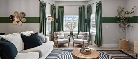 A modern living room with a sofa, two armchairs, a coffee table, and a large window with curtains.