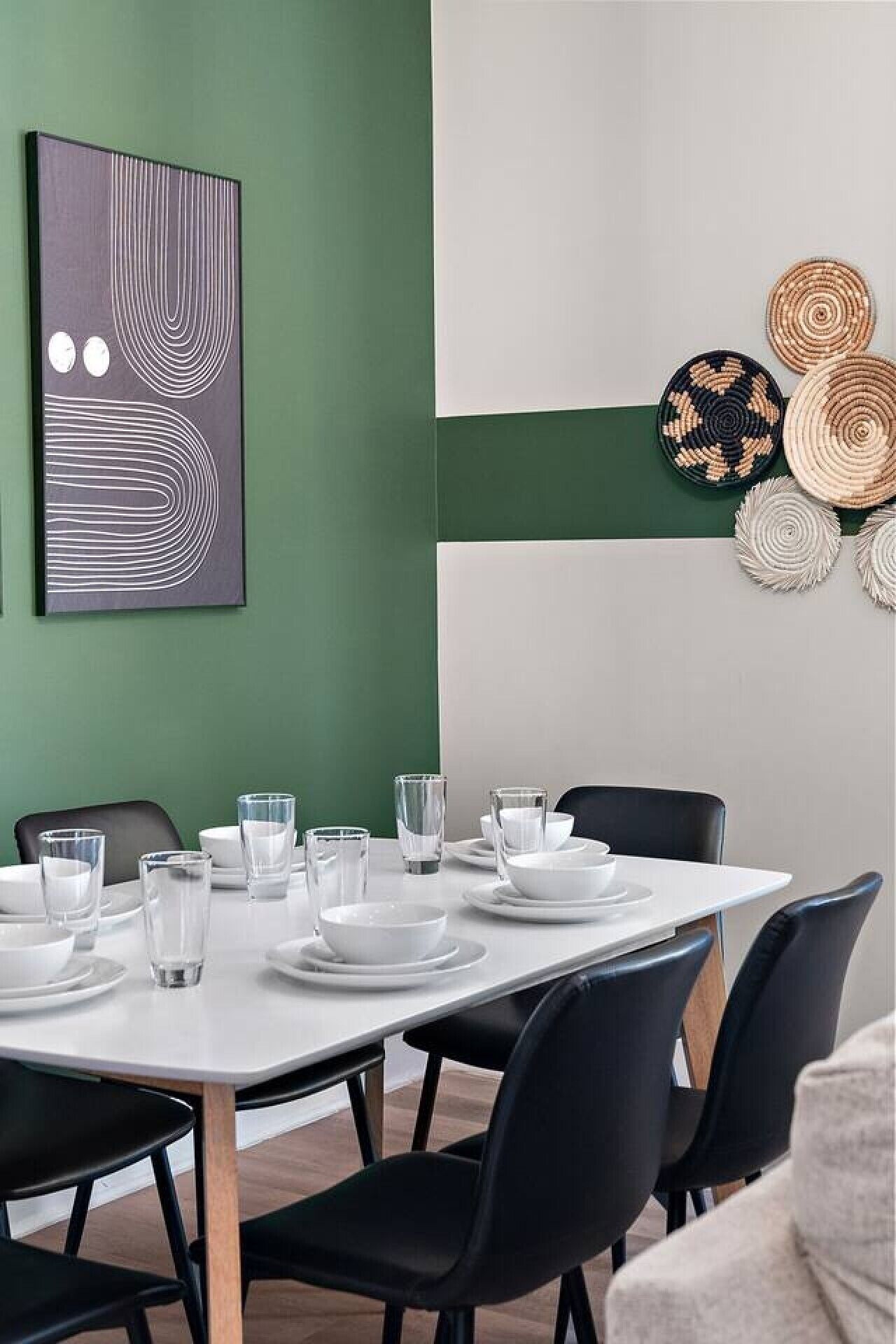 Comedor con una mesa blanca para seis personas, sillas negras y una pared de acento verde.