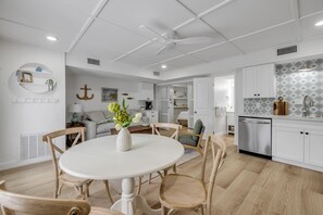 Eine moderne Küche mit weißen Schränken, eine Essecke mit rundem Tisch und Holzstühlen sowie ein Deckenventilator.