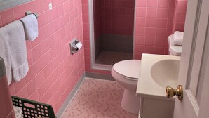 A bathroom with pink and white tiles, a toilet, a shower, and a towel rack. - Room 10-Traditional Motel Room w/Oceanview (Daytona Beach)