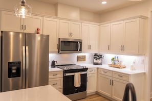 A modern kitchen with stainless steel appliances, white cabinetry, and a built-in microwave. - Ocean Pearl Three Bedrooms (Pensacola)