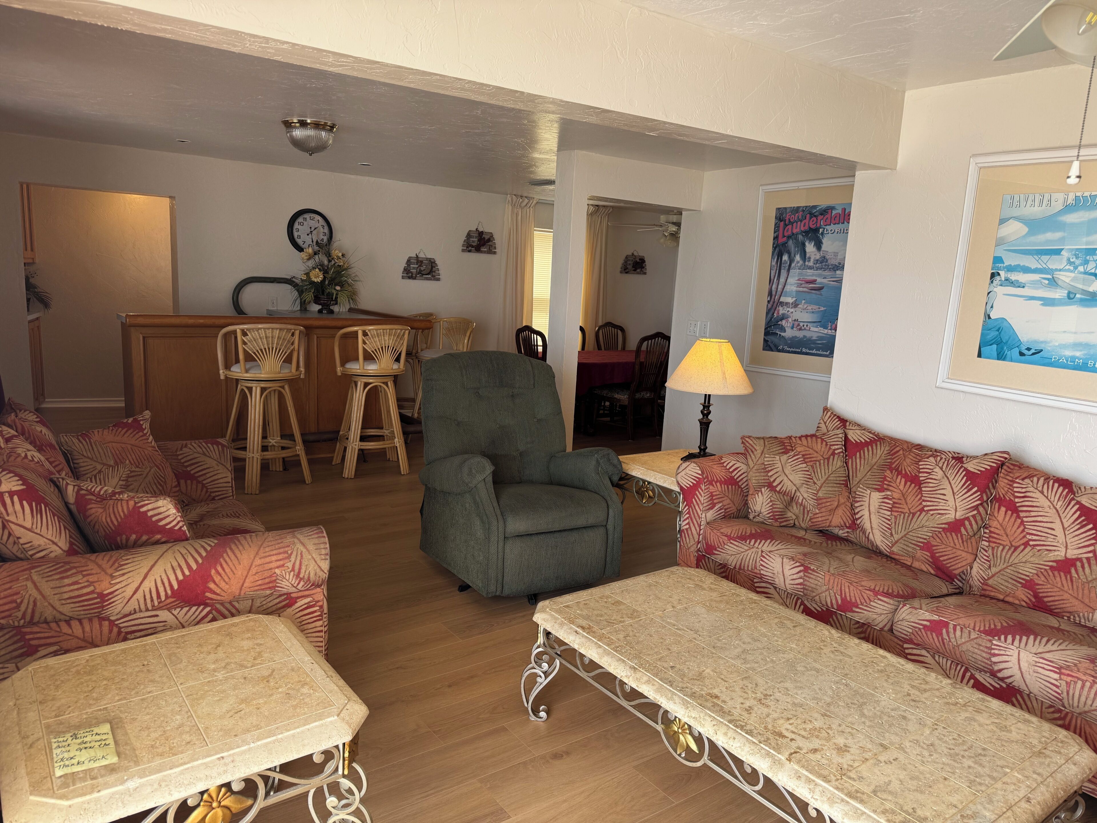 A living room with a sofa, armchair, and a small table. There is a dining area with chairs and a table in the background.
