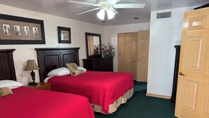 A hotel room with two beds, a ceiling fan, a dresser, a mirror, and a wooden door. - 14-B One bedroom/one bath w/kitchen & living (Daytona Beach)