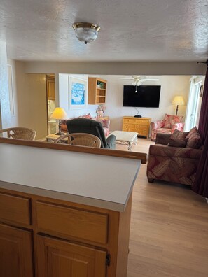 Una sala de estar con televisor, ventilador de techo, mueble de madera y sofá estampado.