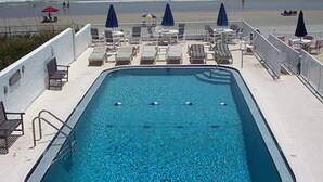 Ein Pool mit Liegestühlen und Sonnenschirmen mit Blick auf einen Strand.