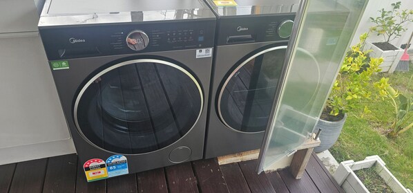 Two Midea front-loading washing machines on a balcony with a view of a garden.